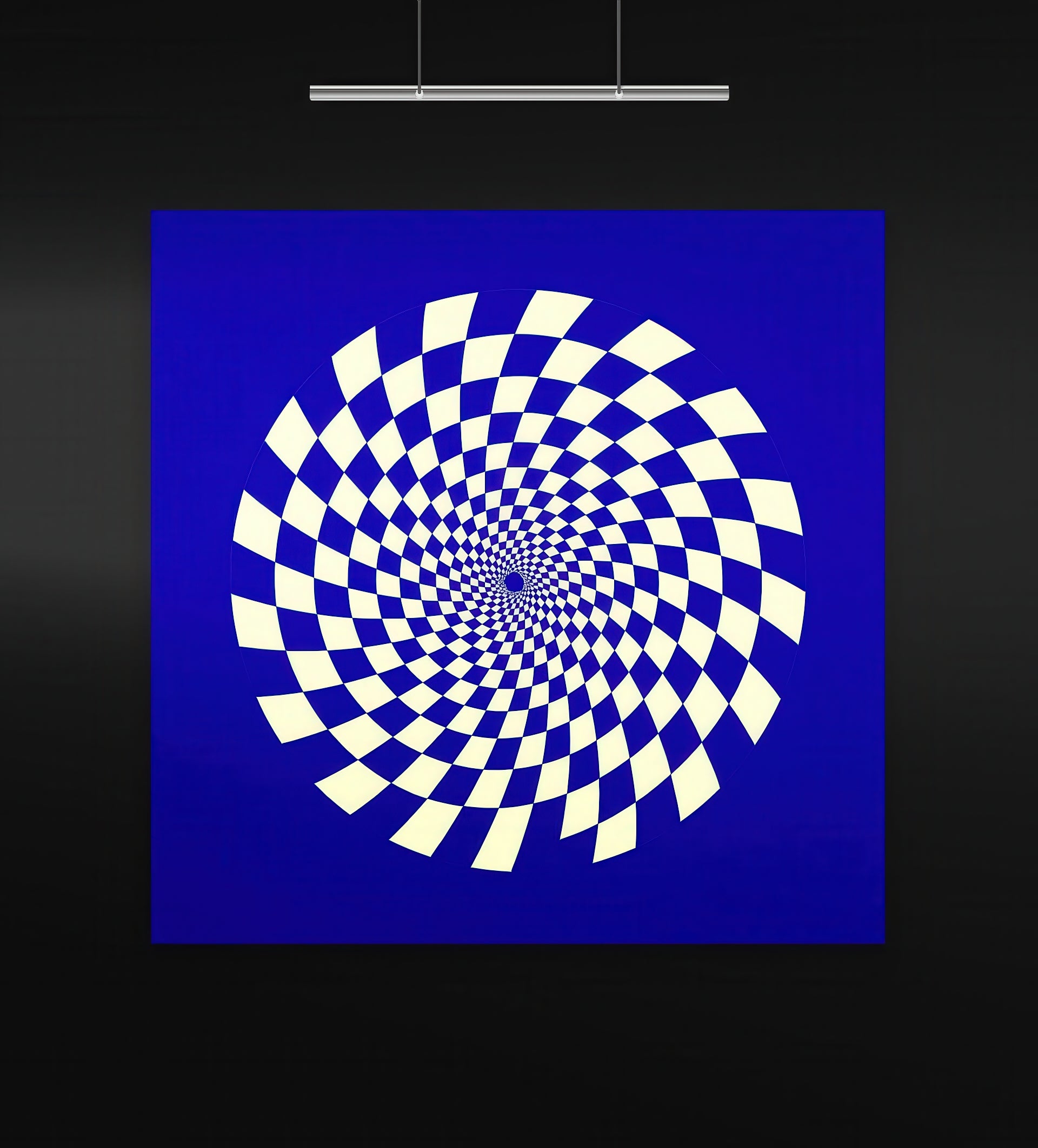 Gravity Bloom (Indigo & Cream) artwork displayed in a black-walled gallery with focused overhead lighting. The square composition features a hypnotic spiral of alternating cream and deep indigo checkerboard tiles, creating an intense optical illusion that draws the eye inward. The bold color contrast emphasizes geometric motion and psychedelic symmetry.